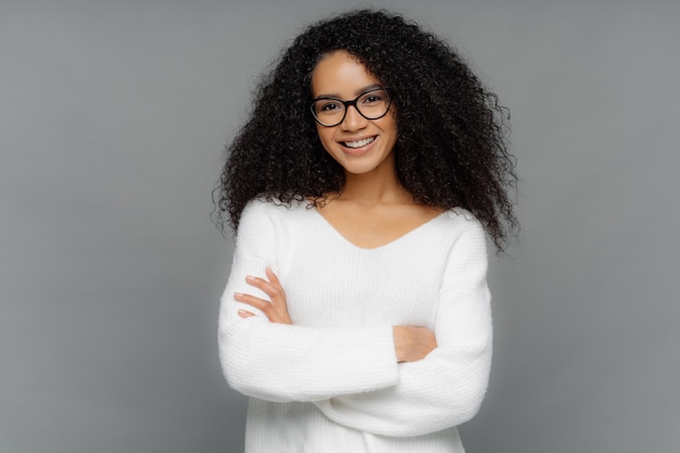 Beautiful African American woman with curls, has gentle smile, keeps hands crossed