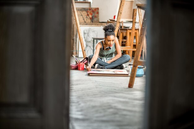 Beautiful african ethnicity student painting on the floor at the university classroom