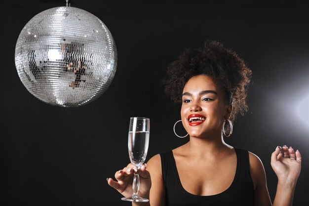 Beautiful african woman standing with silver disco ball isolated over black space