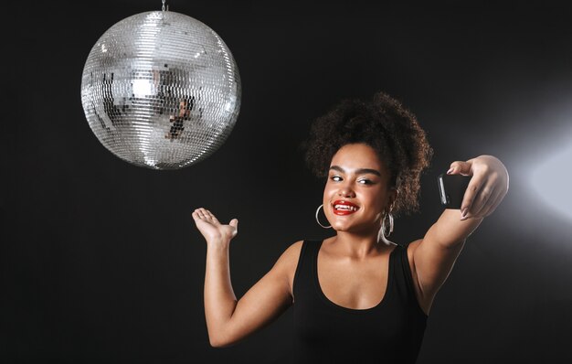 Beautiful african woman standing with silver disco ball isolated over black space