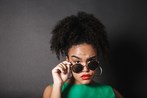 Beautiful african woman wearing sunglasses posing isolated over black space