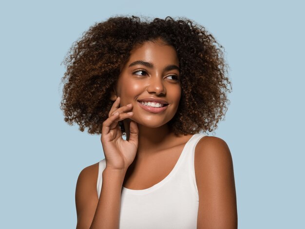 Beautiful african woman white t-shirt portrait afro haircut touching her face Color background blue