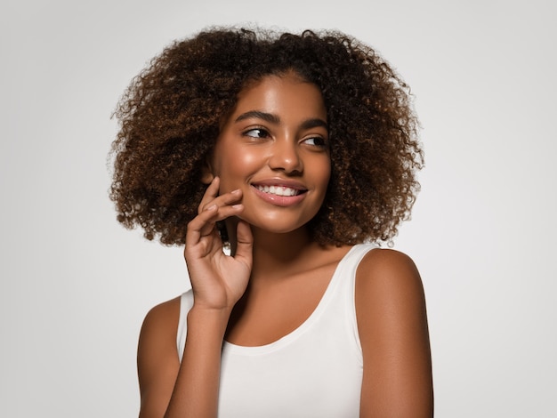 彼女の顔に触れる美しいアフリカの女性白いTシャツの肖像画アフロヘアカット色背景灰色