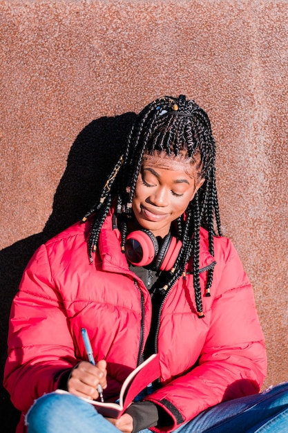 屋外でヘッドフォンを持つ美しいアフリカの女性ノートに書く黒人女性