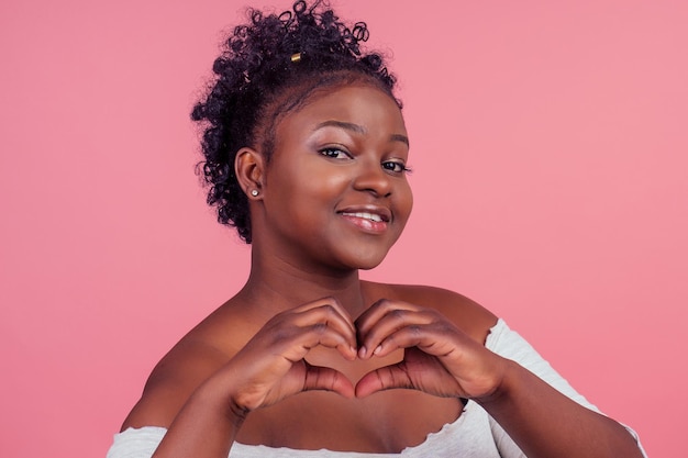 Beautiful african woman with perfect skin curly hair looking at ca,era in pink studio backgtound