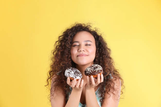 Beautiful AfricanAmerican woman with donuts on yellow background