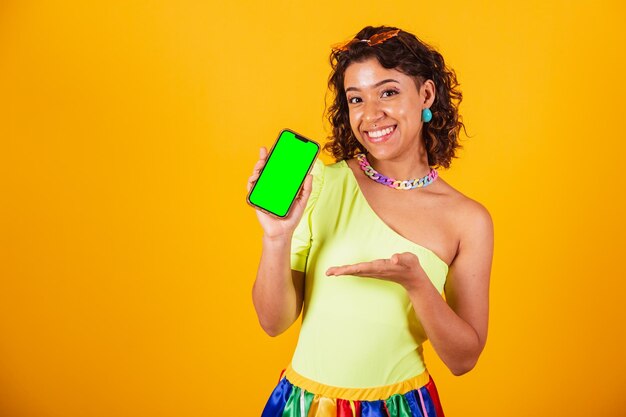 Красивая афро-американская бразильская женщина в карнавальной одежде держит смартфон с зеленым экраном в цветности