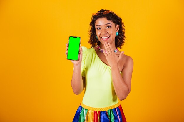 Beautiful afro american brazilian woman in carnival clothes holding smartphone with green screen in chroma