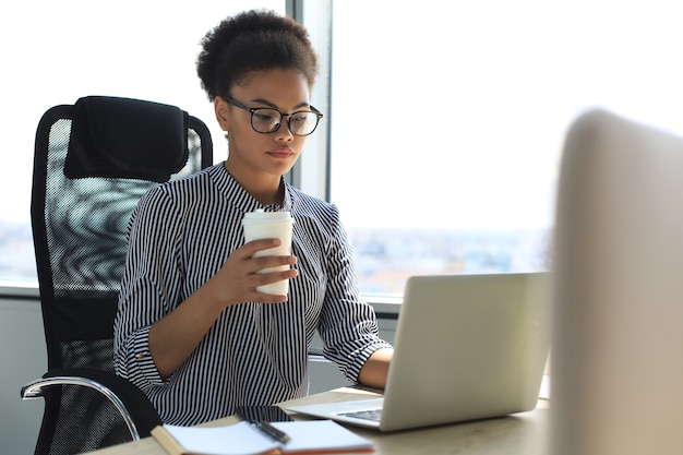 사무실에서 노트북 작업을 하는 스마트 캐주얼 차림의 아름다운 아프리카계 미국인 비즈니스 여성.