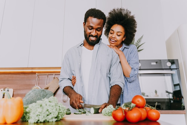 Beautiful afro american couple cooking at home - Beautiful and cheerful black couple preparing dinner together in the kitchen