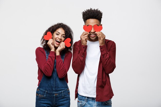 Beautiful Afro American couple holding two red paper heart, looking at camera and smiling