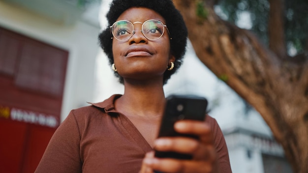 Foto bella ragazza afro che controlla il suo telefono cellulare all'aperto indossando