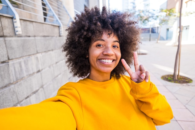 Beautiful afro girl taking a picture with her phone to post it on he social media. Internet and online addiction