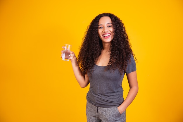 Beautiful afro woman drinking water on yellow background with space for text.