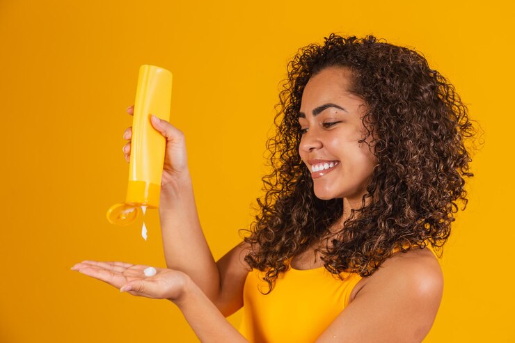 Beautiful afro woman with curly hair applying cream to her hair. Afro woman with hair product in hand