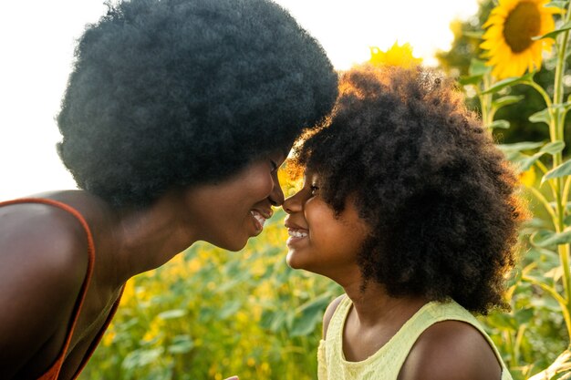 Bella mamma e figlia afroamericane che giocano e si divertono in un campo di girasoli