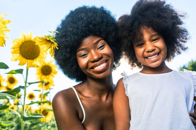 ひまわり畑でおしゃべりして楽しんでいる美しいアフリカ系アメリカ人のお母さんと娘
