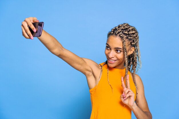 Beautiful afroamerican woman with pigtails doing selfie on colored wall
