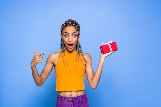 Beautiful afroamerican woman with pigtails and gift box on colored wall