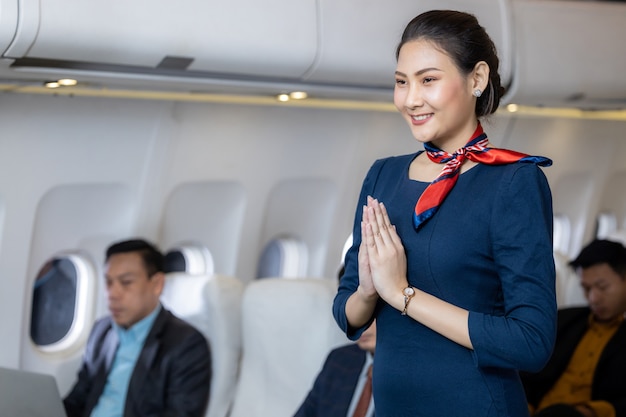 Beautiful air hostess in an airplane smiling, Portrait of asian air hostess posing Sawasdee, Cabin crew or air hostess working in airplane.