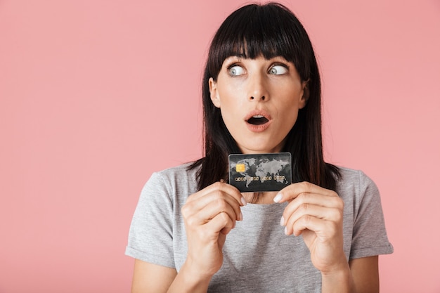 a beautiful amazing excited happy woman posing isolated over light pink wall wall holding credit card.