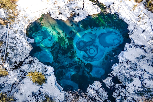 冬の森に囲まれた山の氷のない湖の美しい素晴らしい風景。ガイザー湖はアルタイ山脈の有名なアトラクションです。シベリア、ロシア。上面図、空中図、