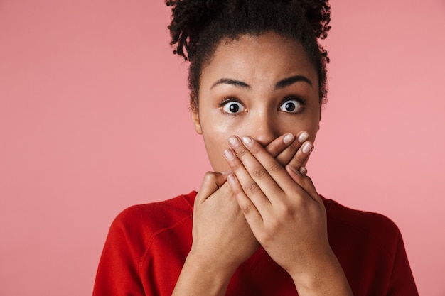 beautiful amazing shocked scared young african woman posing isolated over pink wall covering mouth.