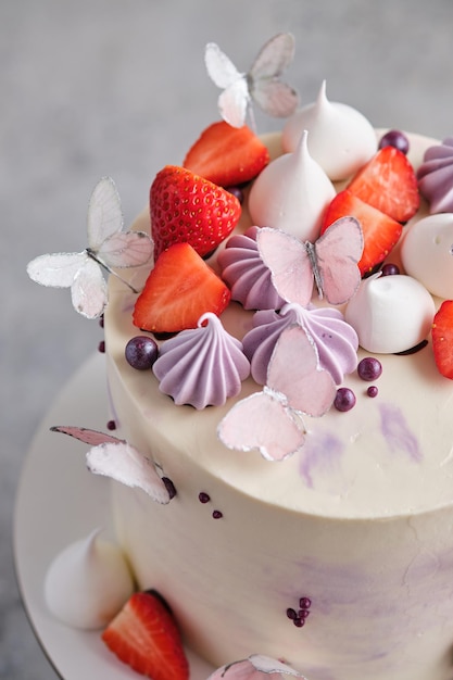 女の子のための美しくて繊細なストロベリーケーキ。デザートは新鮮なイチゴ、メレンゲ、蝶で飾られています。