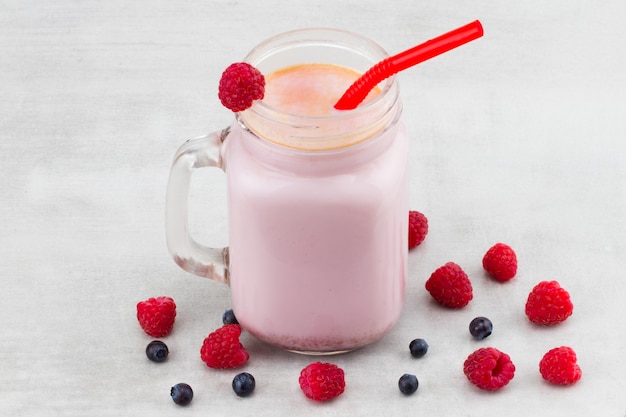 Красивая закуска розовая малина и смузи фруктов черники или молочный коктейль в стеклянной банке с фоном ягод. Йогуртовый коктейль. Закройте вверх.