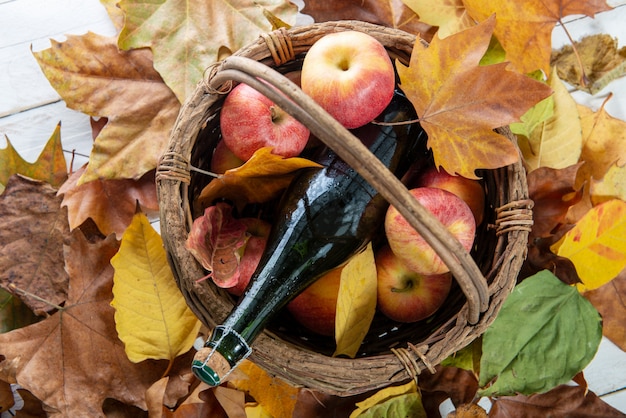 Beautiful apples and bottle of cider, on autumn leaves