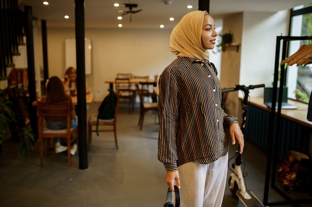 Красивая арабская студентка в хиджабе позирует в университетском кафе. Мусульманская женщина с книгами, сидя в библиотеке.