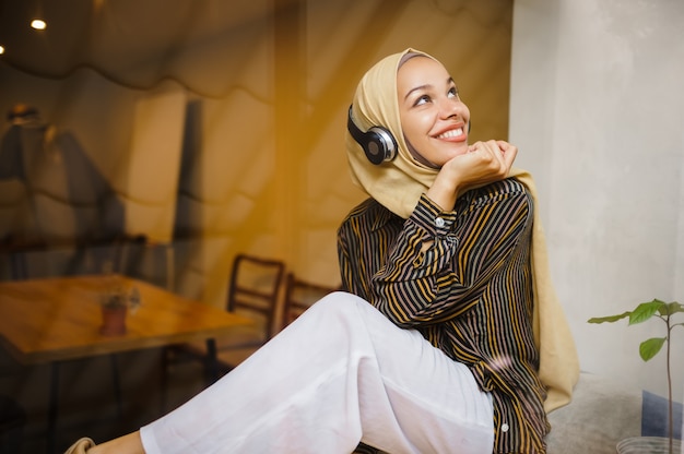 Beautiful arab girl in hijab and headphones in university cafe. Muslim woman with books sitting in library. 