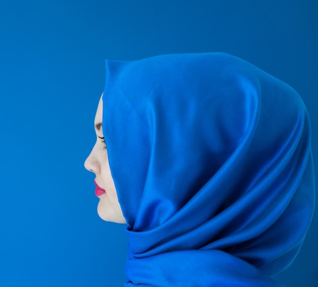 Beautiful Arabic girl with scarf over blue background