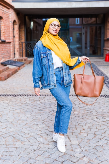 Beautiful Arabic muslim student woman wearing yellow hijab, stylish female portrait over city street