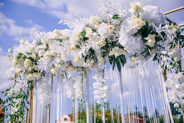 하얀 꽃과 초록잎 리본으로 장식된 푸른 하늘을 배경으로 아름다운 아치형 신혼부부의 포토존