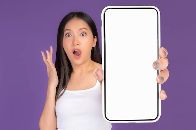 Beautiful Asian brunette woman cute girl in white tank top Excited surprised girl showing big smart phone with blank screen white screen isolated purple background Mock Up Image