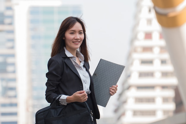 Beautiful asian business woman in black suit with folder of documents in her hands outdoor
