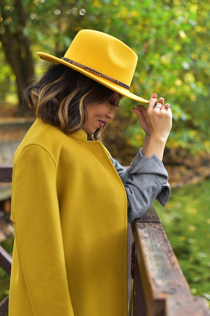 Photo beautiful asian businesswoman in grey suit yellow hat yellow coat in the park close to to lake autumn