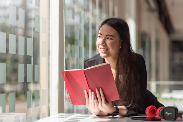 Foto bella donna di affari asiatica che tiene una cuffia del libro un orologio sulla scrivania