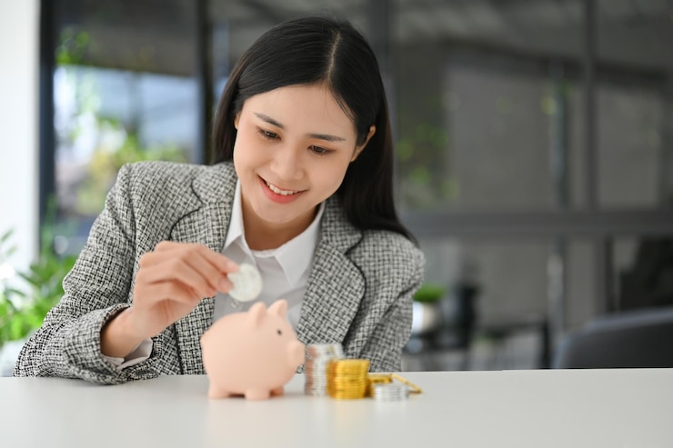 Photo 美麗的亞洲女商人將硬幣放入桌上的粉紅色小豬<unk>中