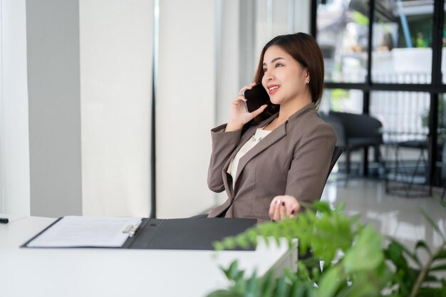 A beautiful Asian businesswoman is talking on the phone with her client while sitting at her desk