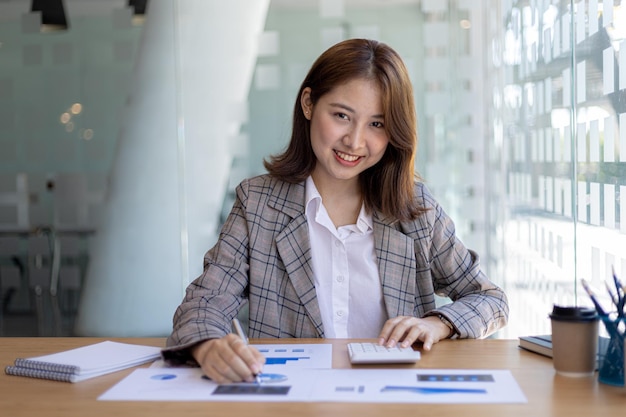 그녀는 개인 사무실에 앉아 회사 재무 문서를 확인하고 있는 아름다운 아시아 여성 사업가입니다. 그녀는 신생 기업의 여성 임원입니다. 재무 관리의 개념입니다.