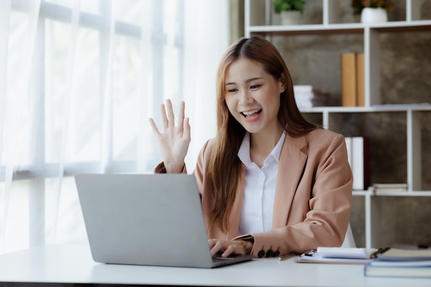 Beautiful Asian businesswoman sitting in her private office she is talking to her partner via video call on her laptop she is a female executive of a startup company Concept of financial management