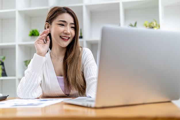 Beautiful Asian businesswoman sitting in her private office, she is talking to her partner via video call on her laptop, she is a female executive of a startup company. Concept of financial management