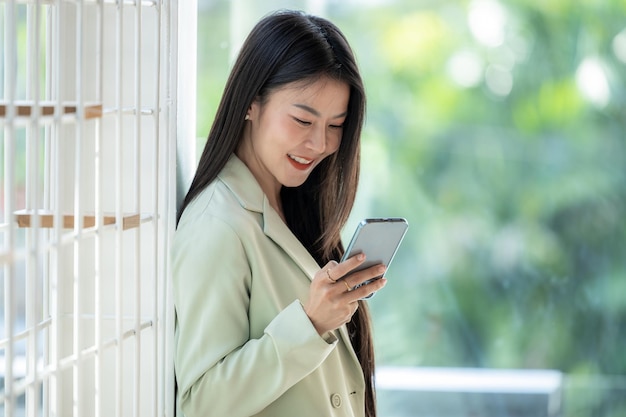 Bella donna d'affari asiatica sorridente e utilizzando lo smartphone che lavora sorriso bella donna asiatica d'affari con un vestito che lavora in ufficio utilizzando lo smartphone donna d'affari asiatica felice che utilizza il telefono cellulare