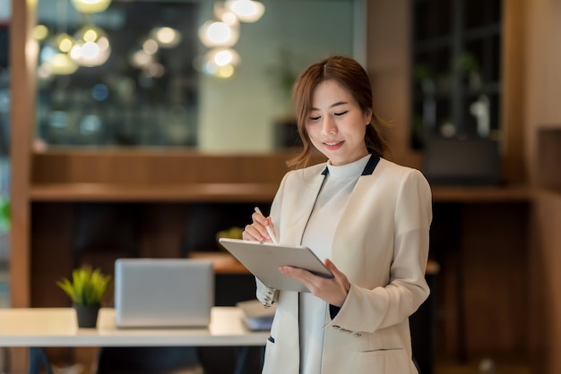 Beautiful Asian businesswoman standing holding a digital tablet at the office.