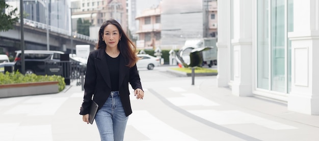 아름다운 아시아 여성 사업가는 태블릿을 들고 도시 거리를 걷는 검은 양복을 입습니다. 여자 프리랜서 라이프 스타일 인간의 도시입니다. 텍스트 단어에 대 한 공간 사용을 복사 합니다.