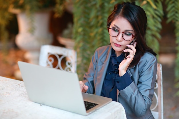 Bella donna d'affari asiatiche con gli occhiali lavorando su computer portatile e telefono cellulare