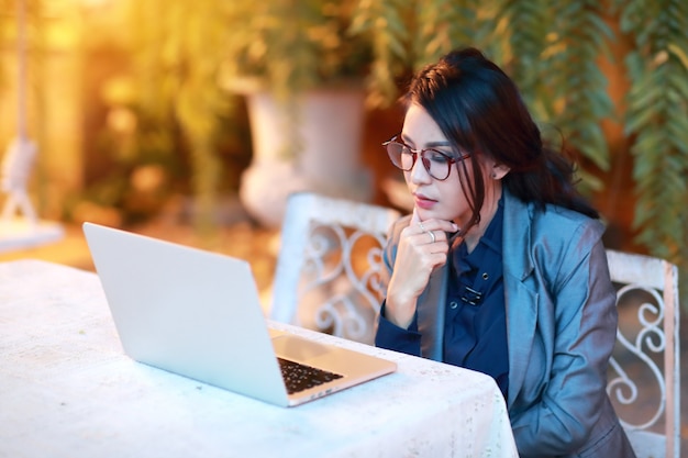 Bella donna d'affari asiatiche con gli occhiali lavorando e pensando sul computer portatile