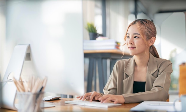 Bella donna di affari asiatica che lavora al suo computer desktop all'ufficio